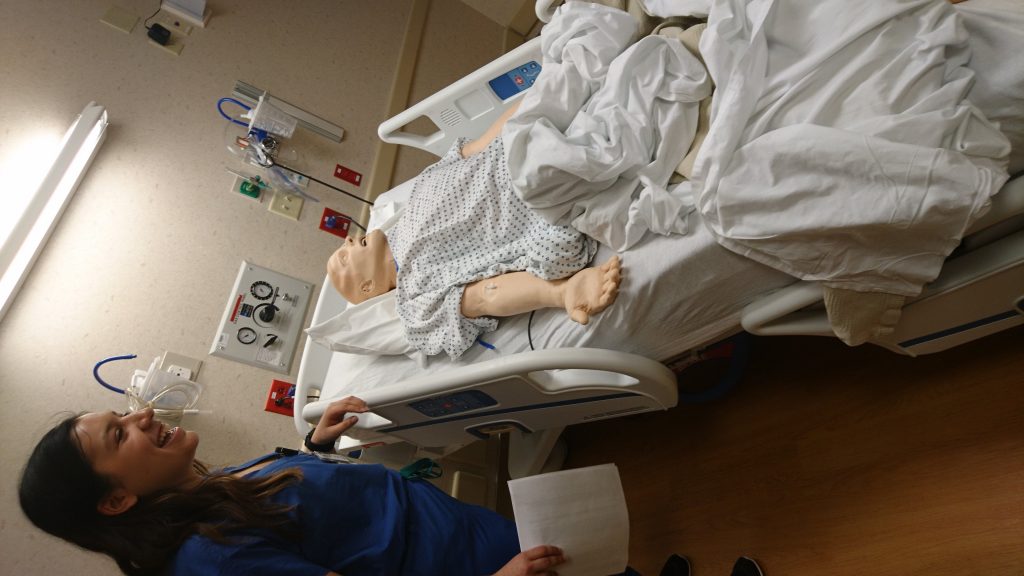 A nurse explains a presentation with a gurney bed occupied by a mannequin